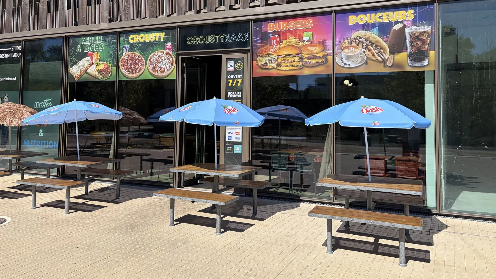 La terrasse de Crousty Naan allée Boutaut : tables en bois et parasols au soleil